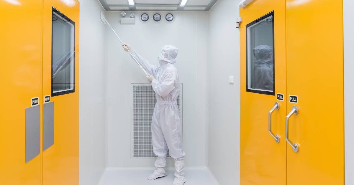 Someone wearing coveralls while cleaning a wall with a long tool. Two sets of orange doors are nearby.