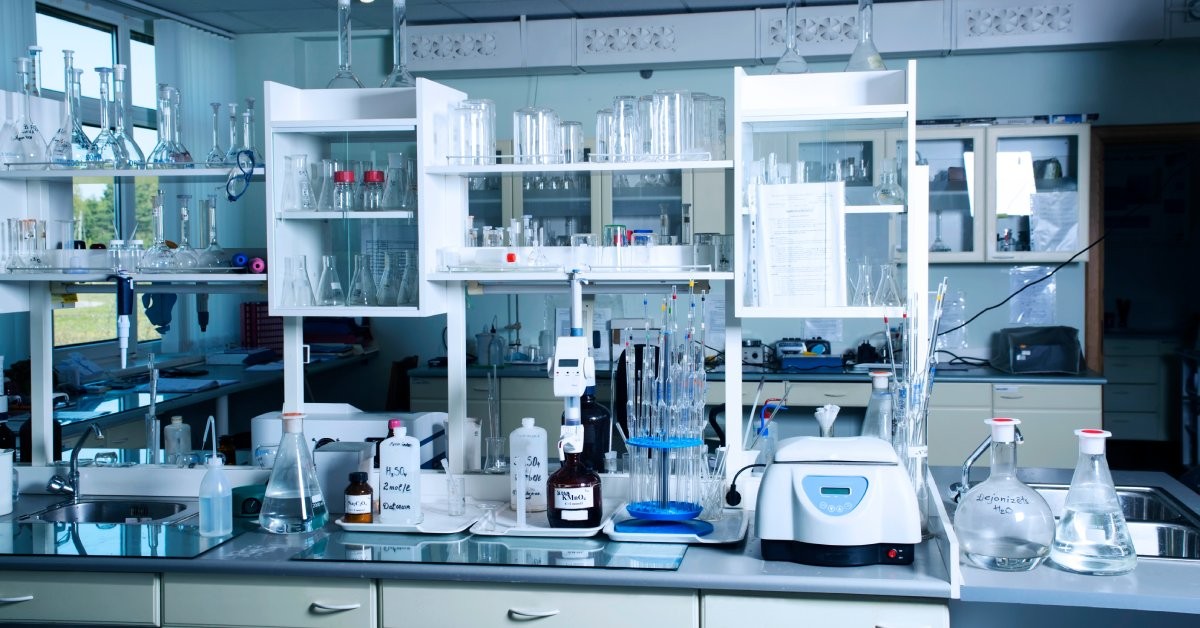 A large laboratory that has white shelves and gray desktops full of equipment, bottles, and beakers.