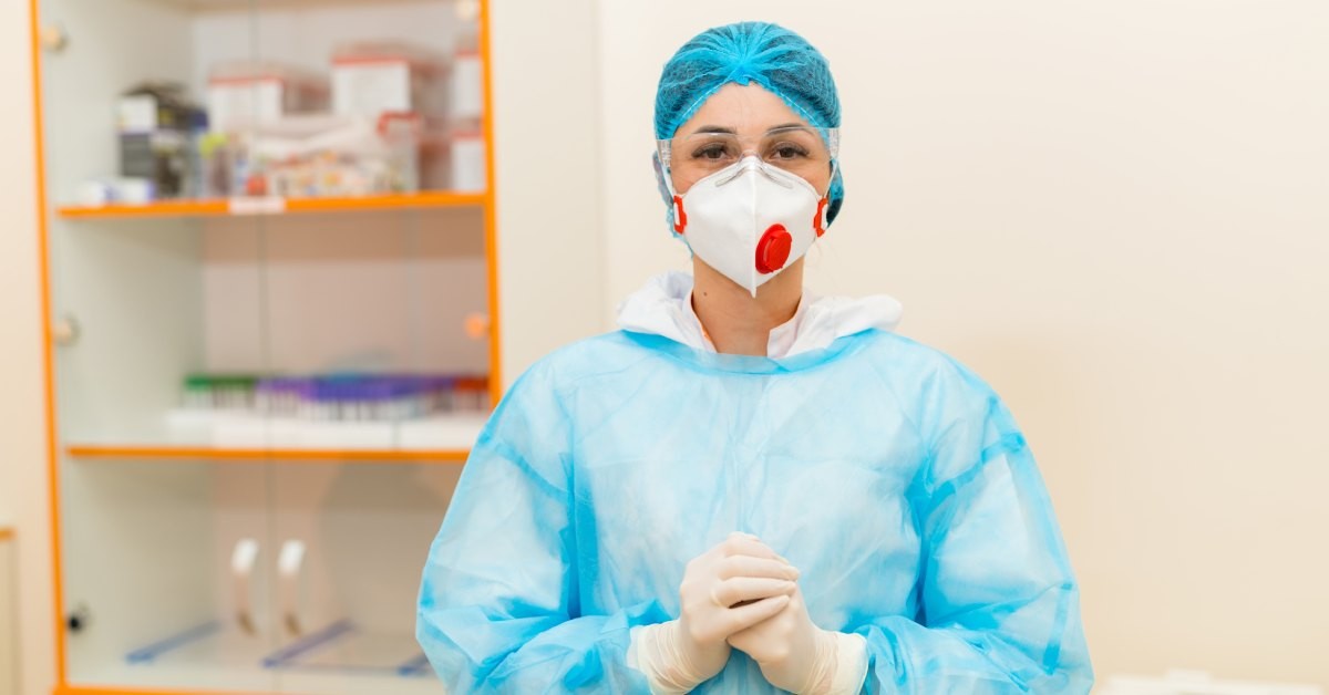 A professional in a lab is wearing a blue uniform. They stand in front of a large cabinet with an orange frame.
