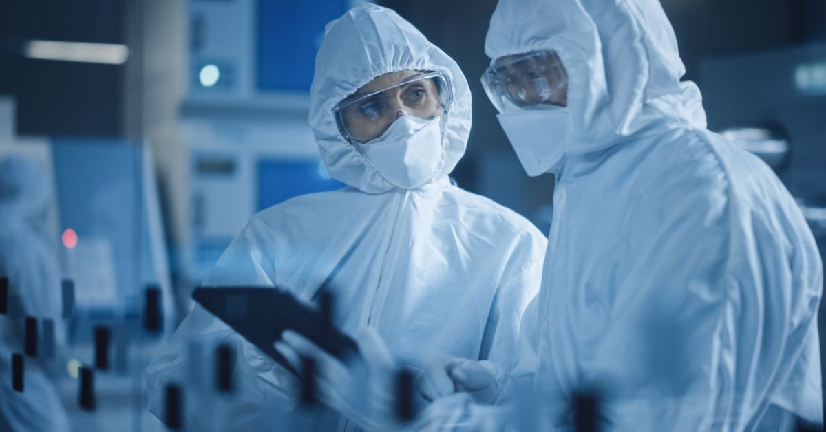Two professionals wearing white lab gowns and safety goggles are standing in a dimly lit laboratory.