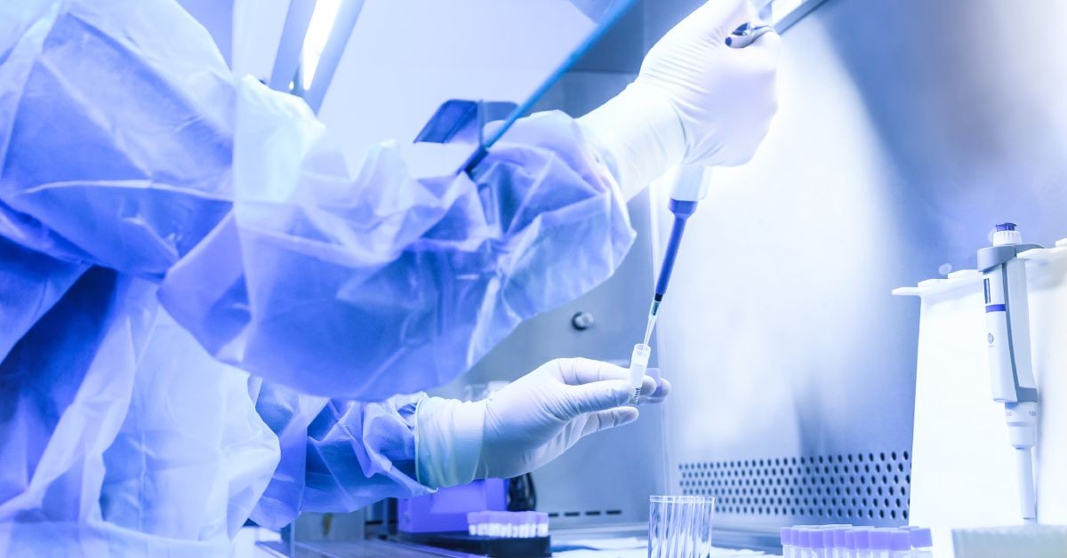 A professional in a laboratory is using a slim device to insert a material into a small vial under a blue light.