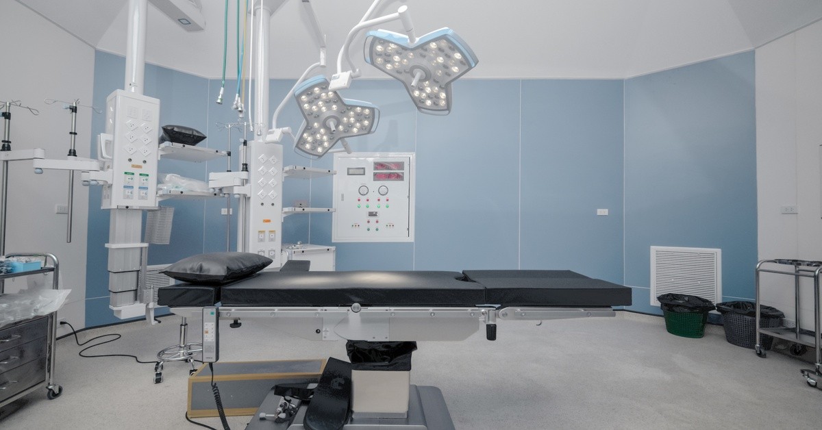 A large empty operating table in a brightly lit hospital room. Two large lights are above the operating table.